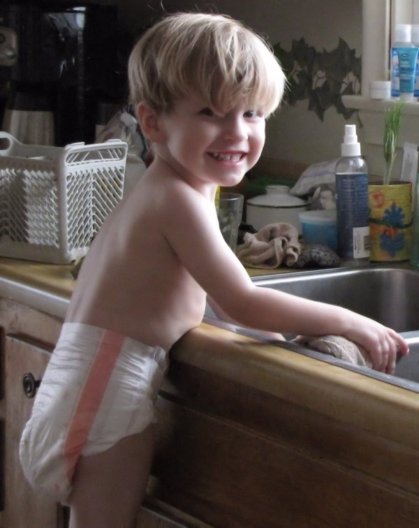 3 year old boy wearing just his diaper and doing dishes