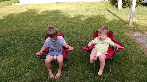 Picture of toddler brothers sitting in camp chair outside in yard wearing diaper and shirt
