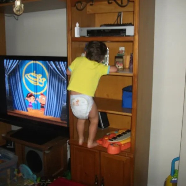 3 year old boy in his pampers and shirt climbing shelf