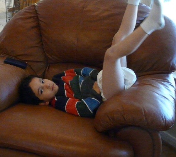 7 or 8 year old boy wearing diaper and shirt laying in chair